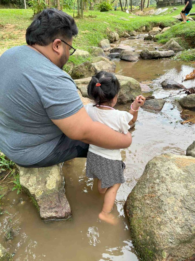 Toddler and dad play in a stream at TTDI Park, a must-see in KL.