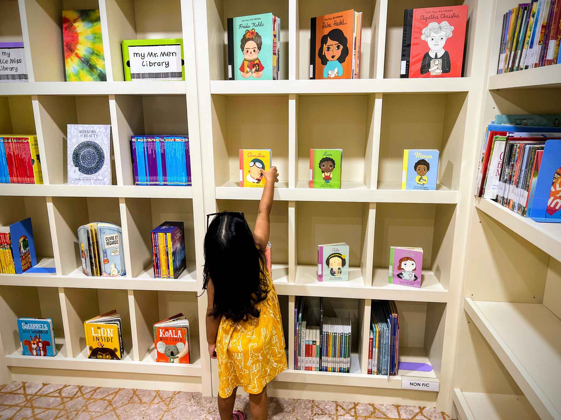A toddler in Malaysia with family reaches for a book in a library.