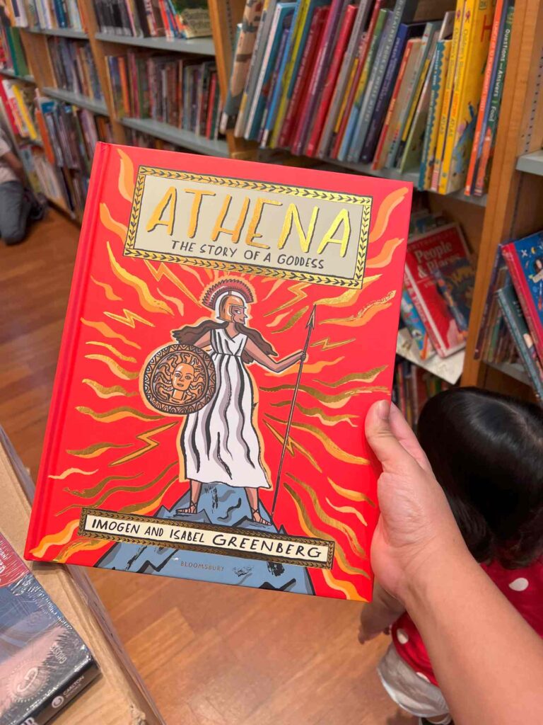 A hand holding up a book on Athena at Kinokuniya KLCC.